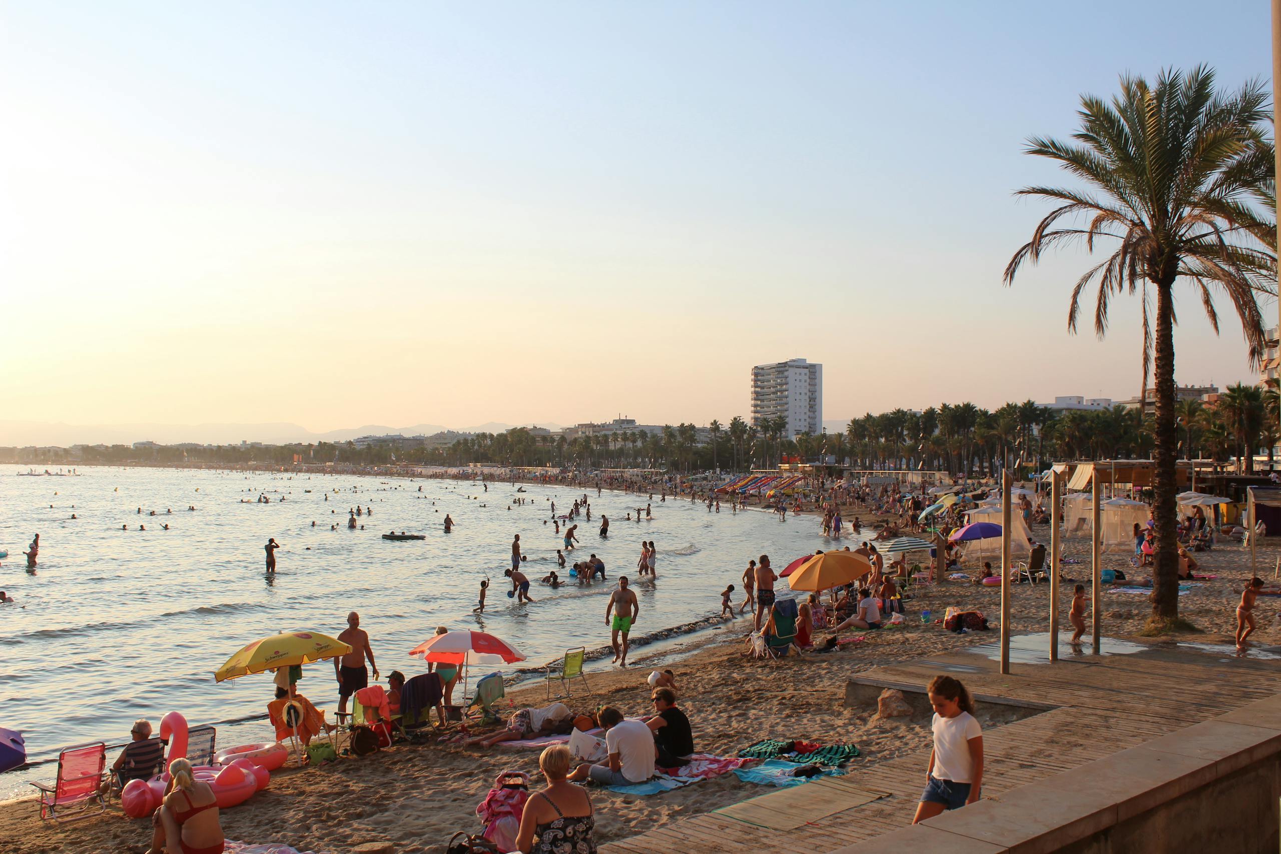 Crowded beach in Spain with people enjoying a sunny day at the shore.