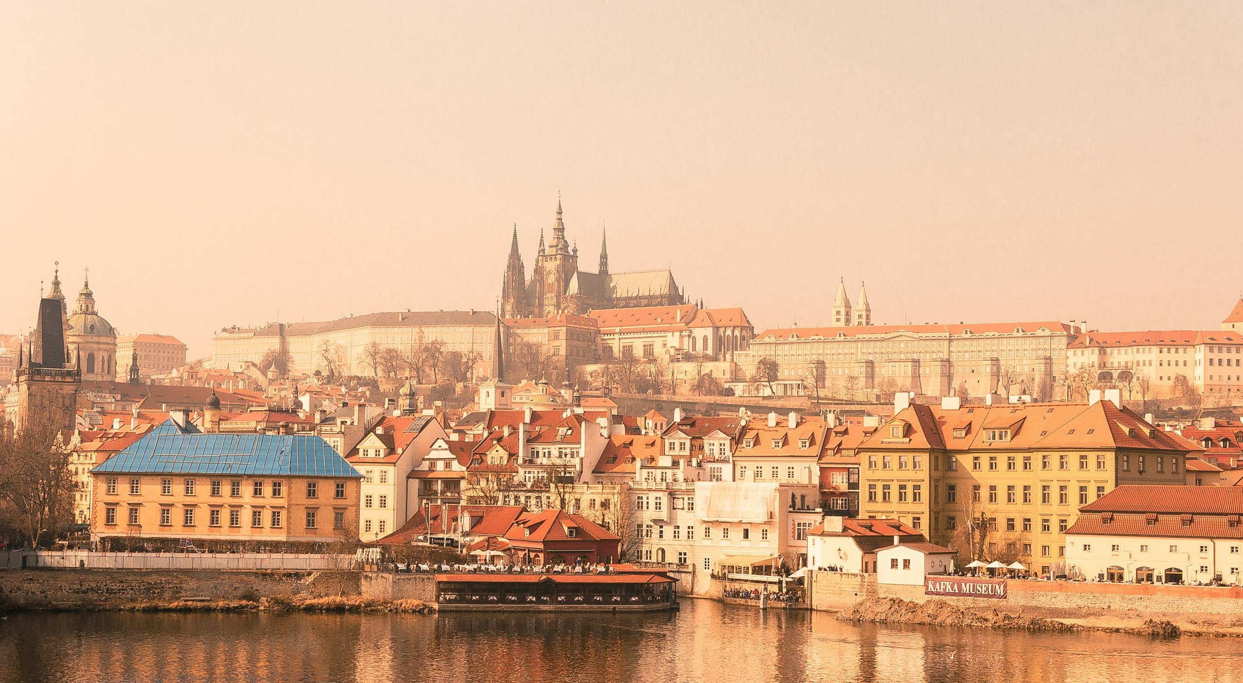 Prague Castle with historic buildings reflected in the Vltava River on a foggy day.
