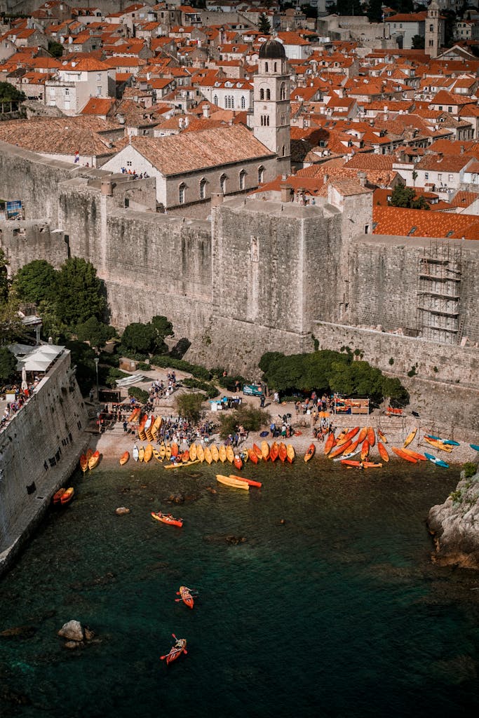 Scenic aerial view of Dubrovnik's stone walls and vibrant kayaks by the turquoise Adriatic Sea.