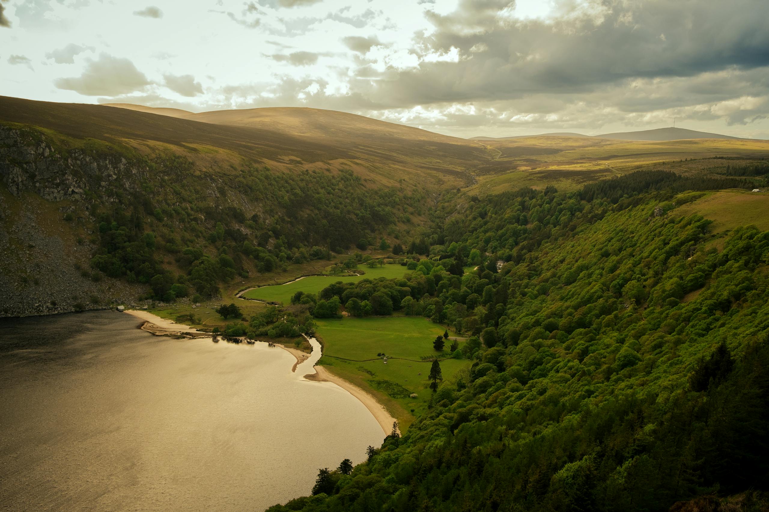 A breathtaking aerial view of a tranquil valley with lush greenery, a river, and mountains in County Wicklow, Ireland.