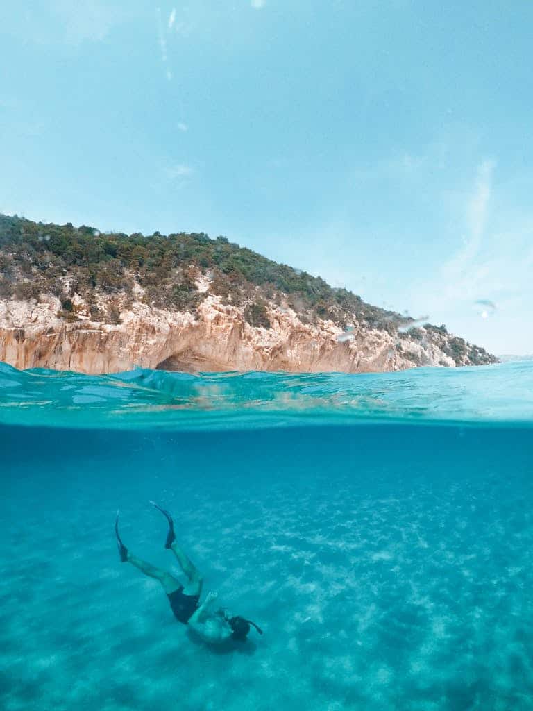 A serene over-under photograph capturing a diver exploring the turquoise waters off the coast of Sardinia, Italy.