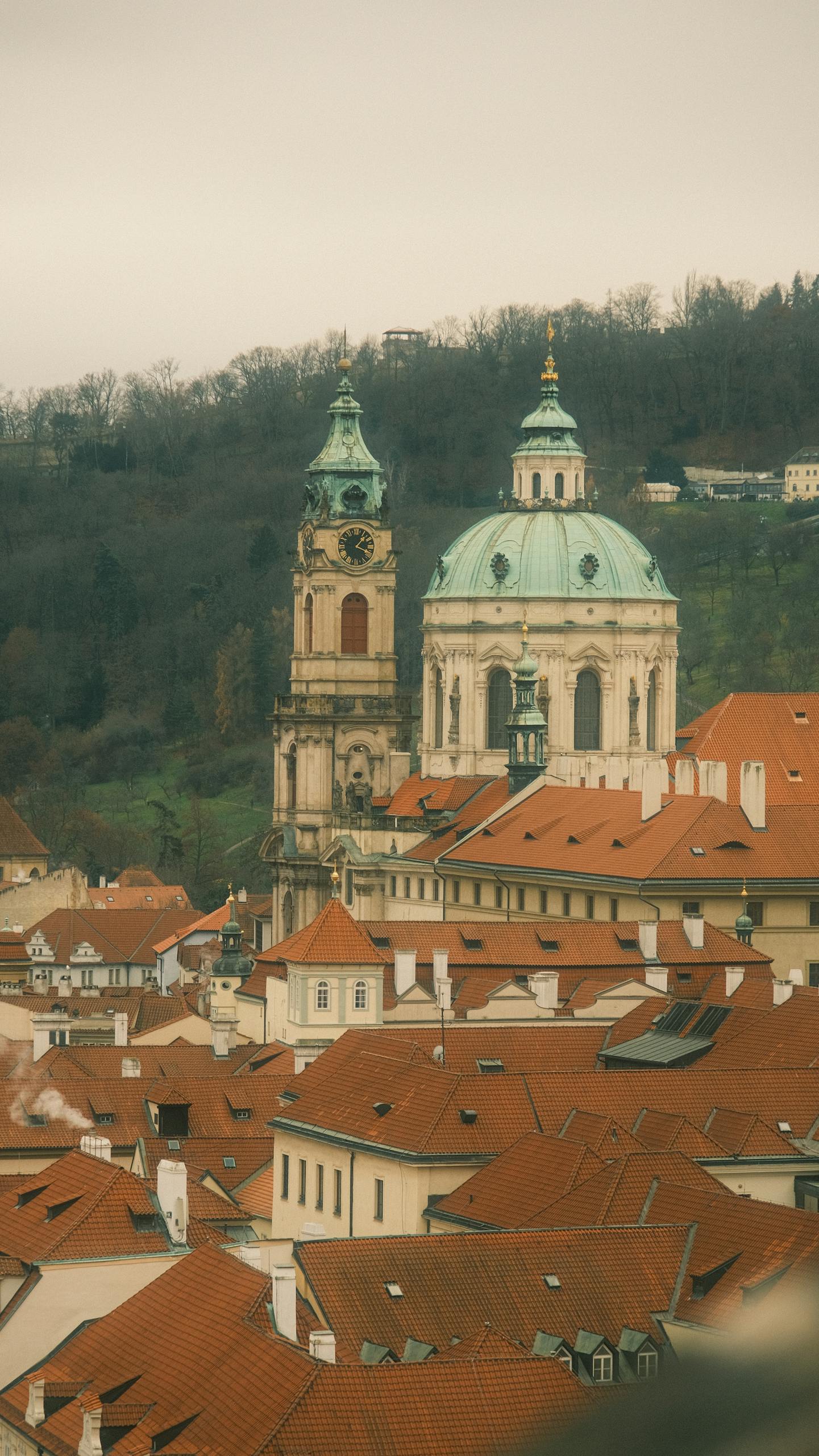 Aerial view of St. Nicholas Church with red rooftops in Prague, nestled in early spring foliage.