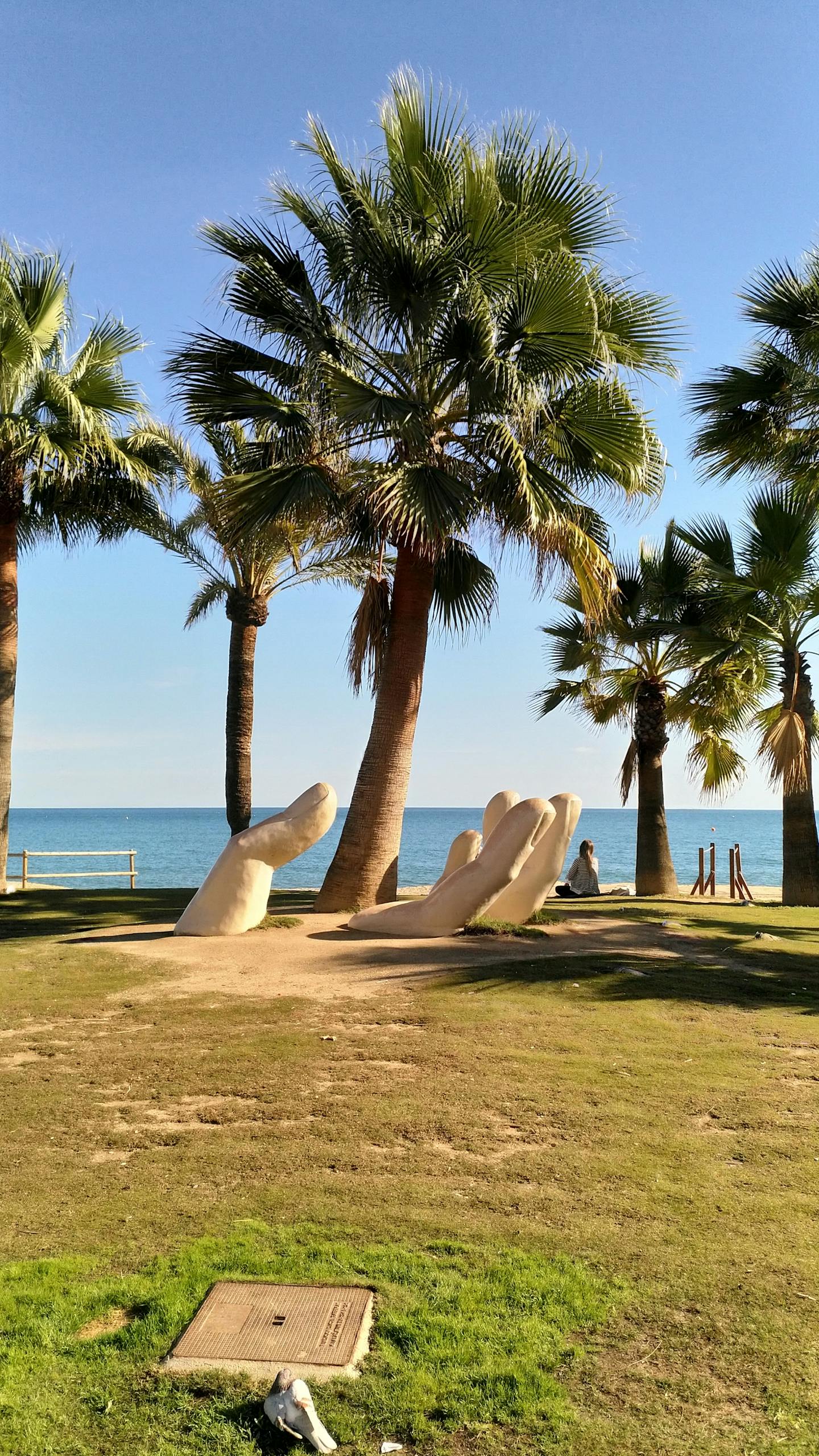Artistic sculpture of hands surrounded by palm trees on a sunny beach in Fuengirola, Spain.