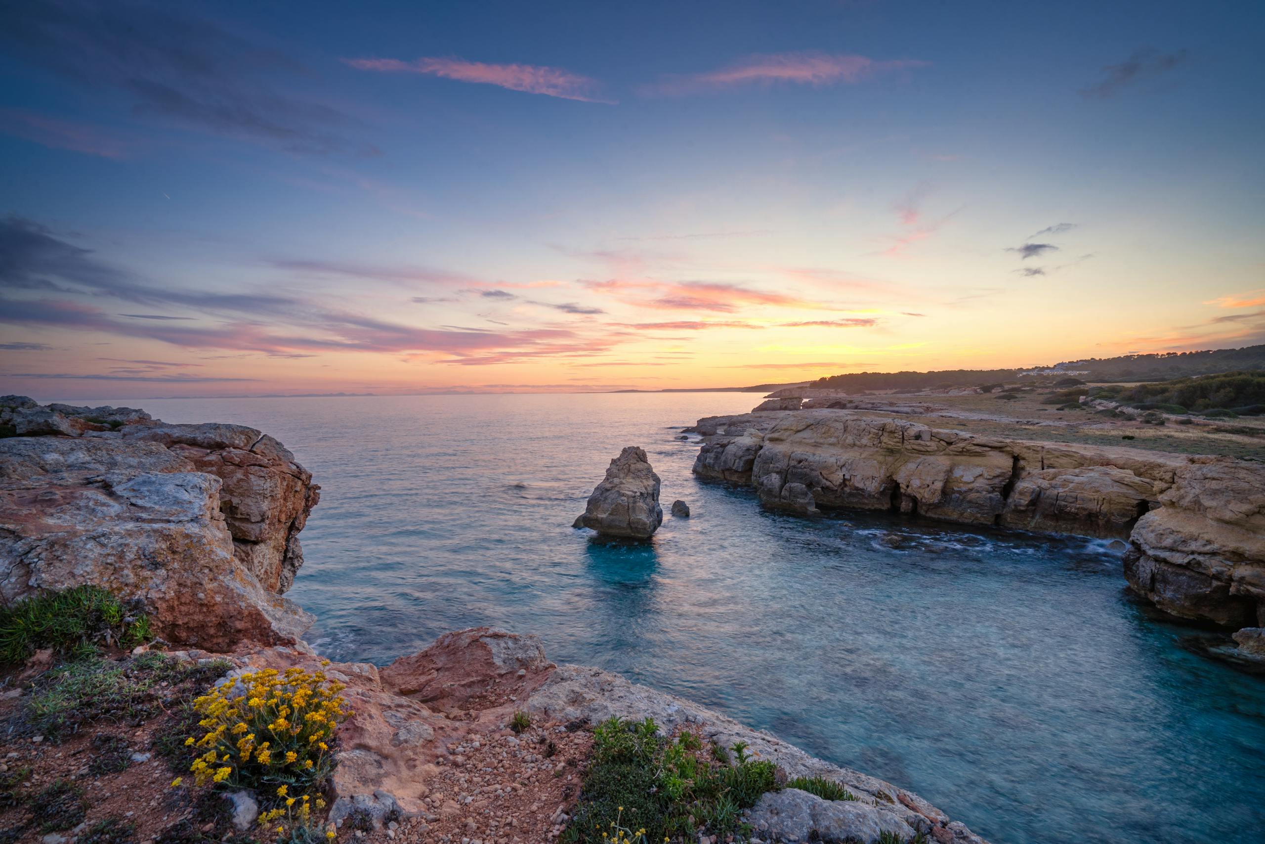 Beautiful sunset over the rocky shore of Ciutadella de Menorca, showcasing vibrant colors.
