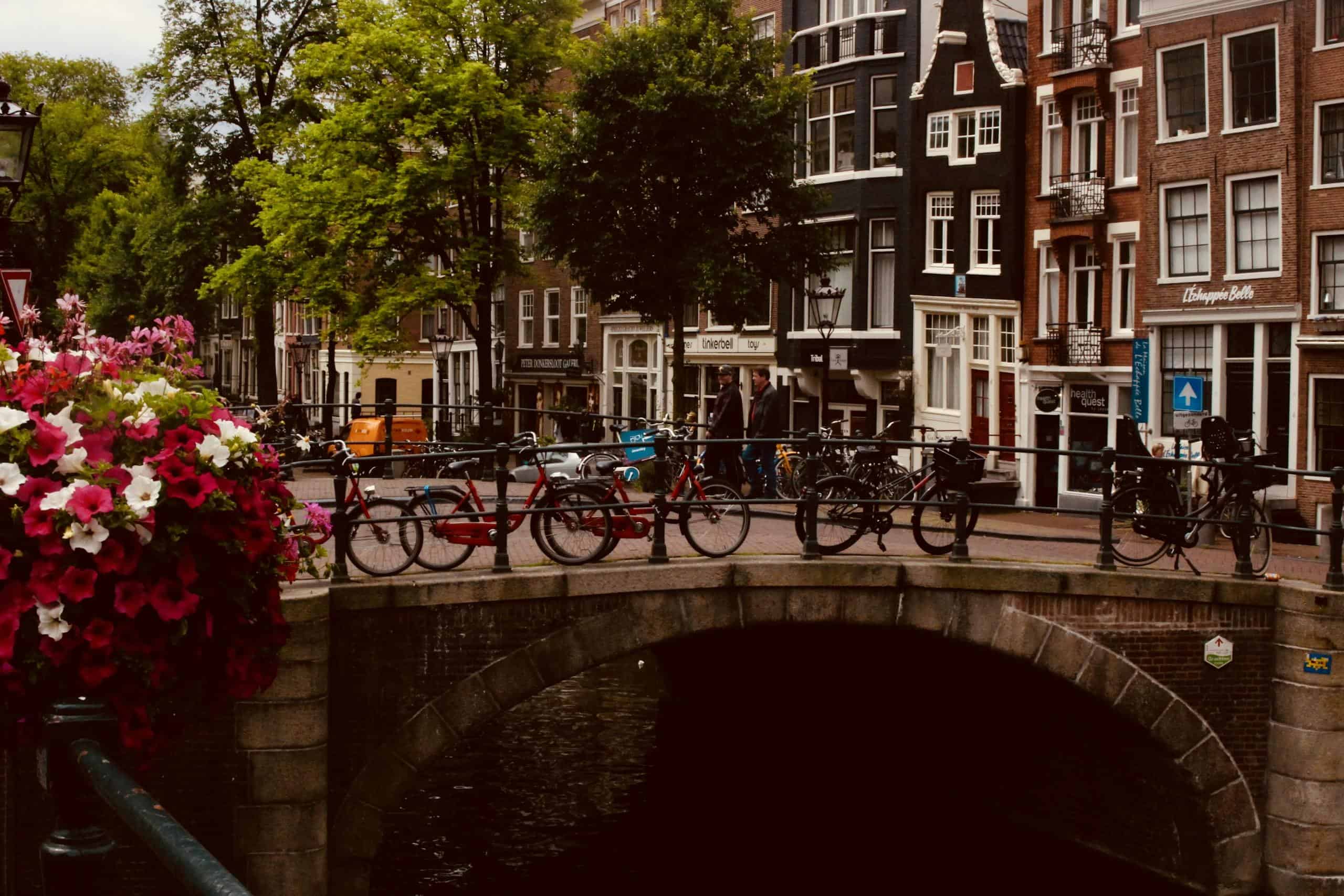 Scenic view of an Amsterdam canal bridge adorned with bicycles and vibrant flowers, perfect for urban travel inspiration.