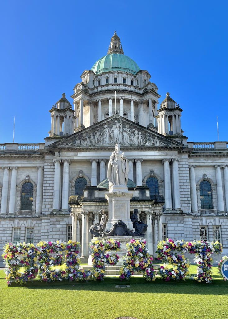 Stunning view of Belfast City Hall with vibrant floral displays under a clear blue sky.