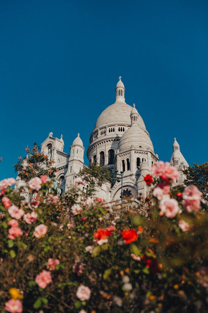 Stunning view of Sacré-Cœur Basilica framed by colorful flowers in Paris, under a clear blue sky.