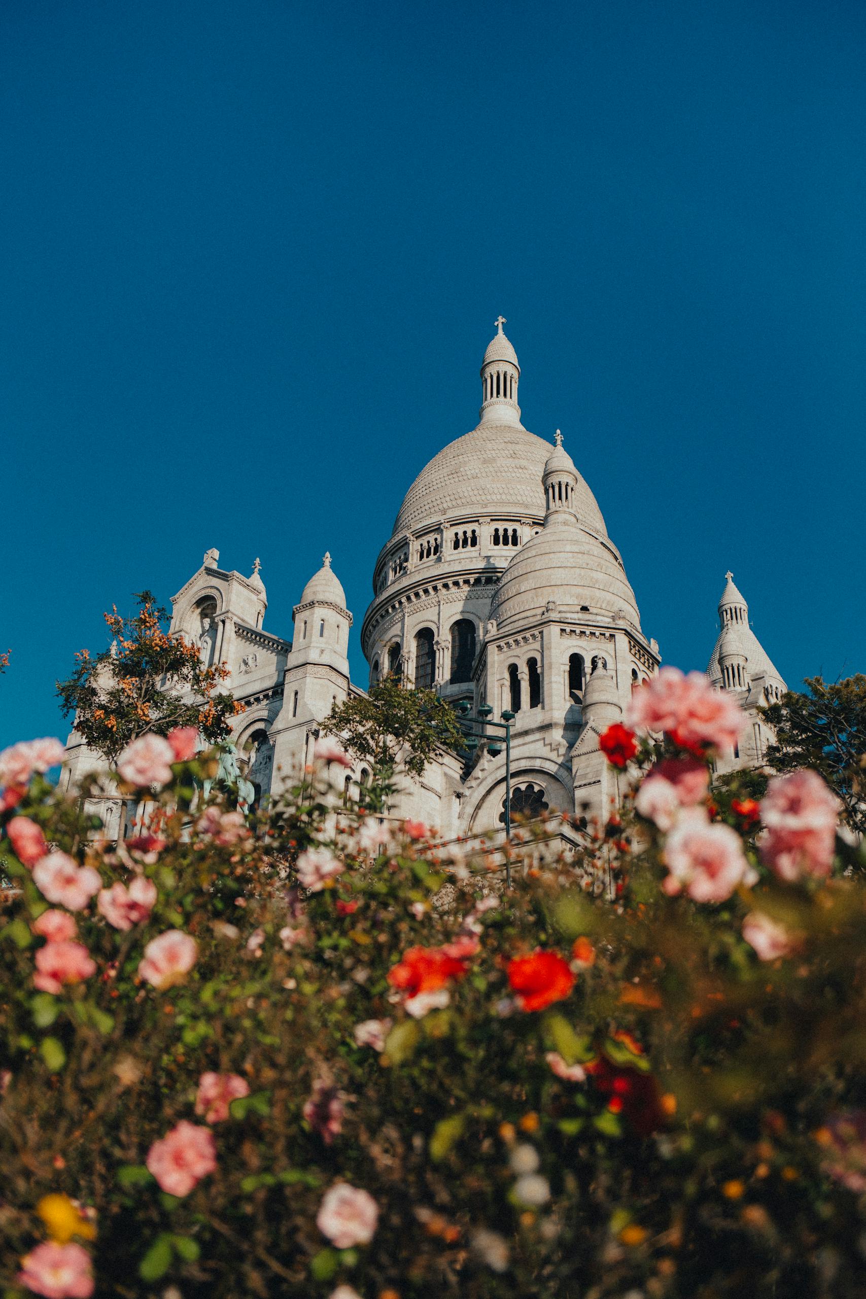 Stunning view of Sacré-Cœur Basilica framed by colorful flowers in Paris, under a clear blue sky.