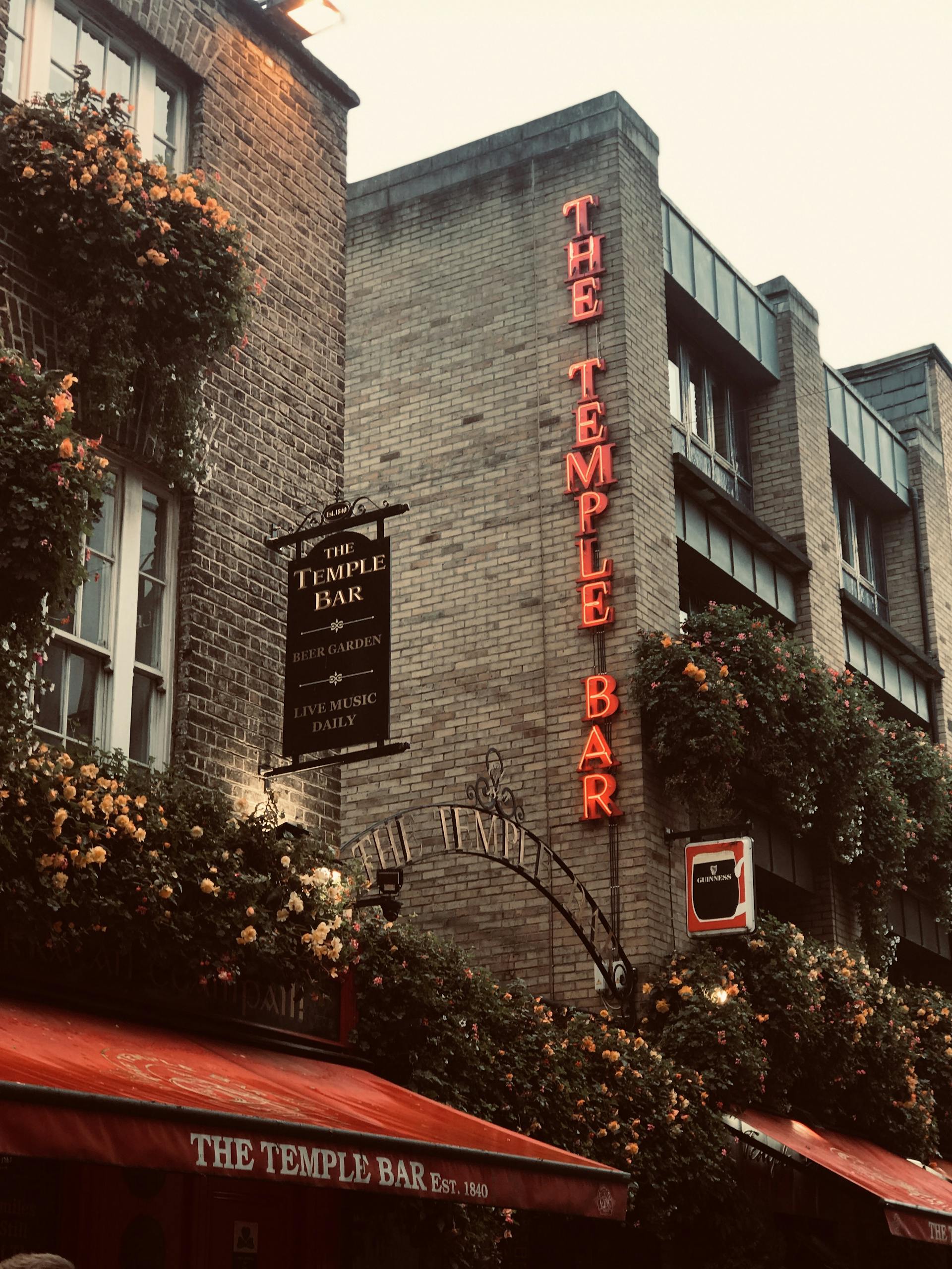 The vibrant facade of The Temple Bar in Dublin is adorned with flowers and neon signage, capturing its lively atmosphere.