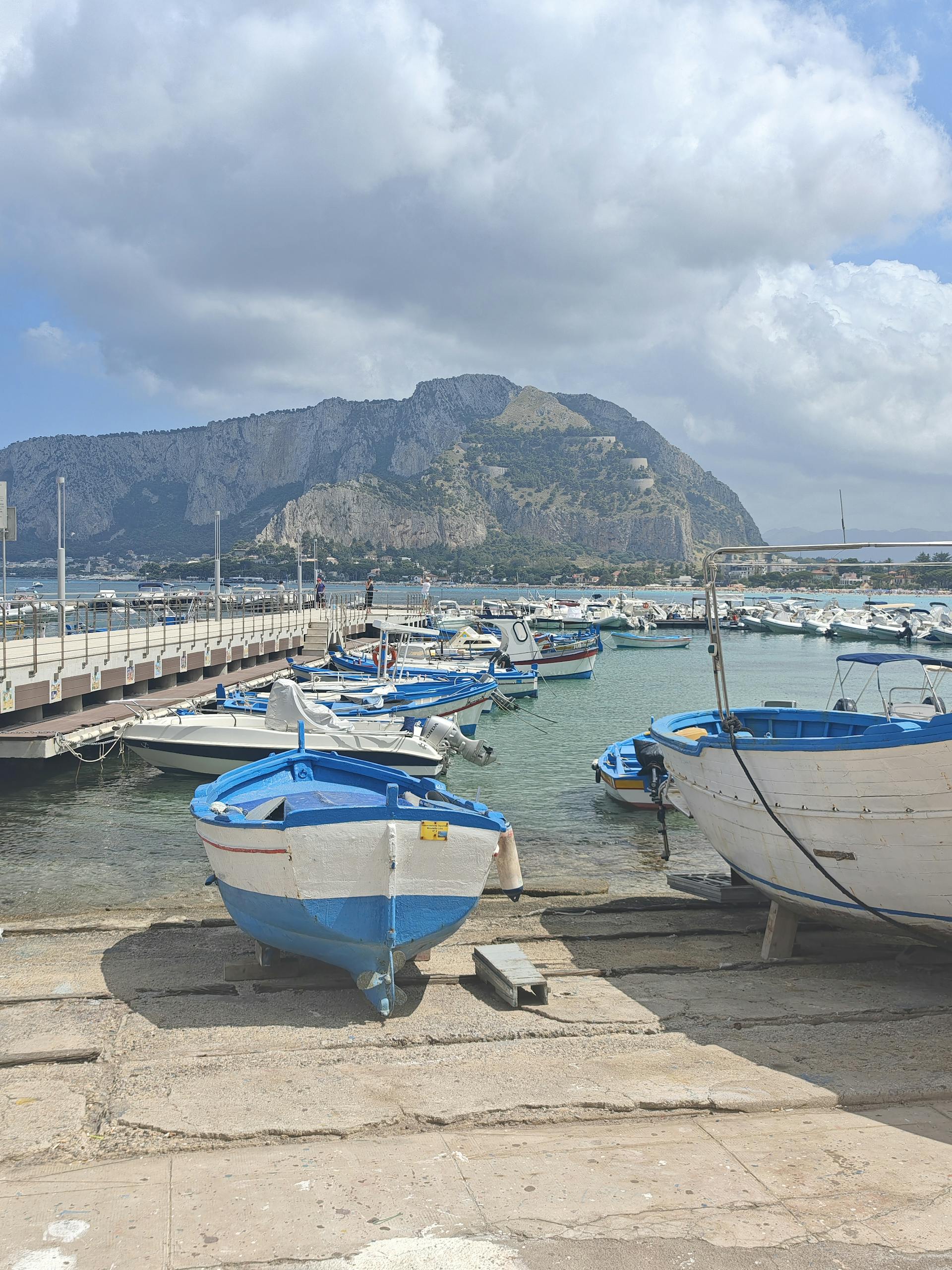 A serene harbor with boats docked against a backdrop of mountains under a cloudy sky.