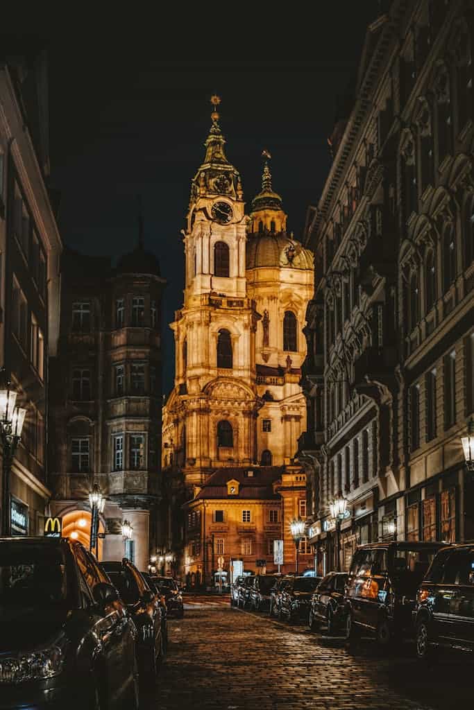 Stunning nighttime view of a Prague street with a beautifully illuminated church as the centerpiece.