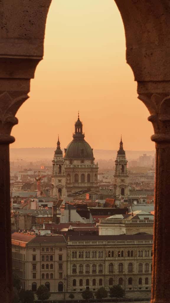 View of St. Stephen's Basilica at sunset framed by Fisherman's Bastion arch in Budapest, Hungary.