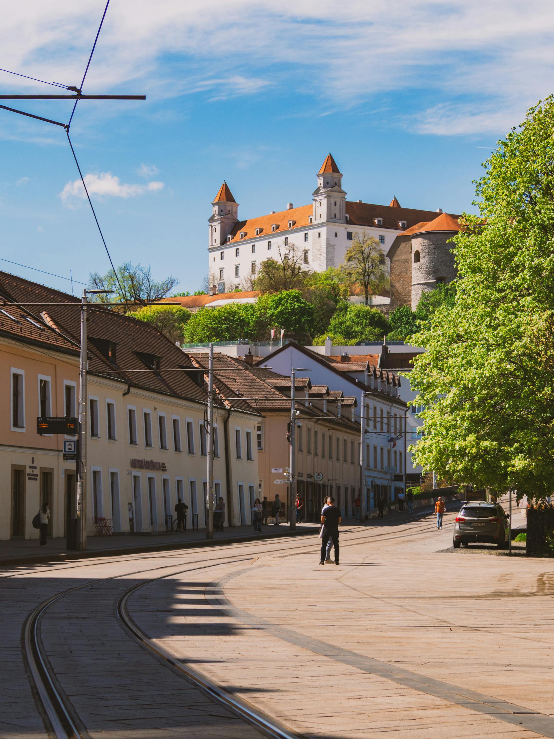Scenic view of Bratislava Castle from a quaint street, showcasing springtime beauty in Slovakia.