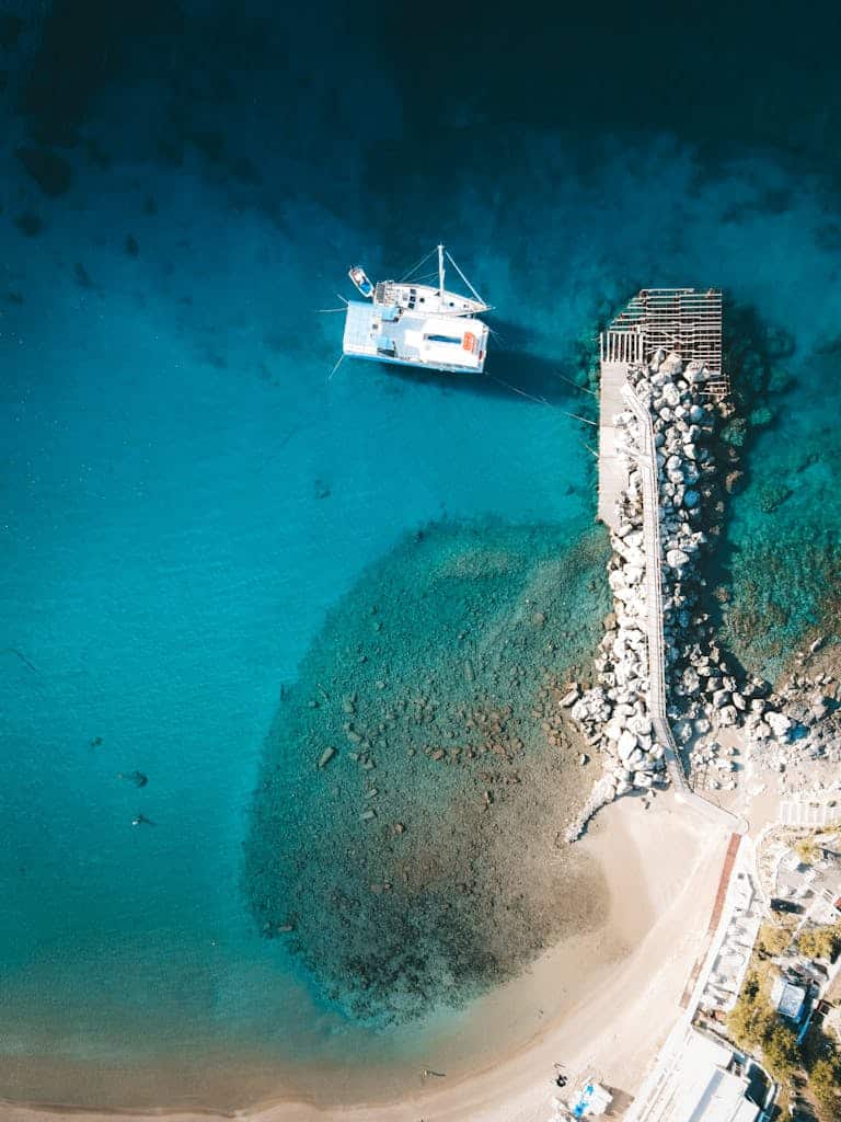 Stunning aerial shot of a catamaran docked at Lindos, Greece, with turquoise waters and rocky pier.