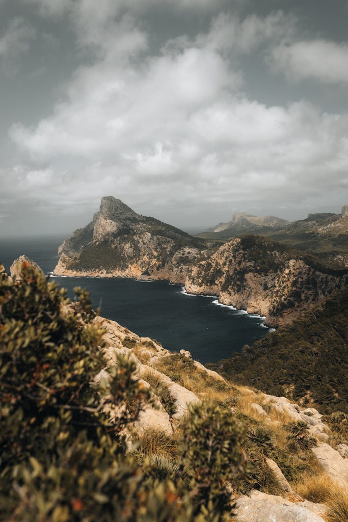 A breathtaking aerial view of Mallorca's rugged cliffs and serene coastline under a cloudy sky.