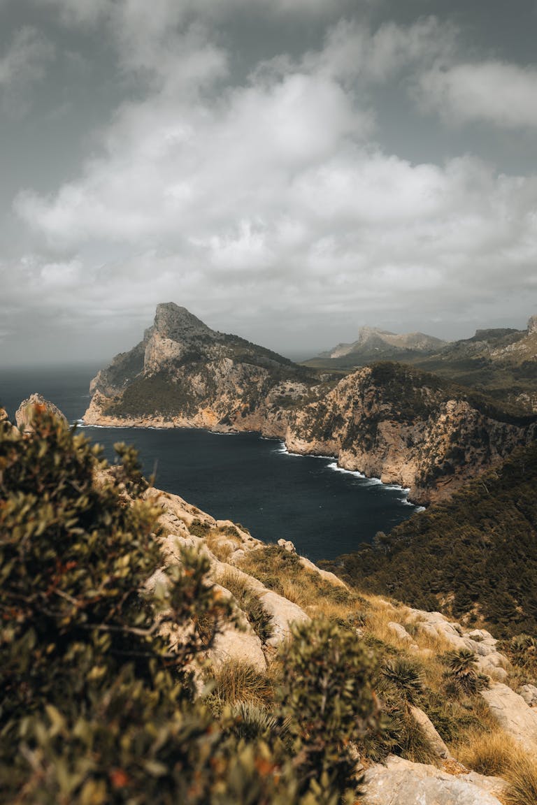 A breathtaking aerial view of Mallorca's rugged cliffs and serene coastline under a cloudy sky.