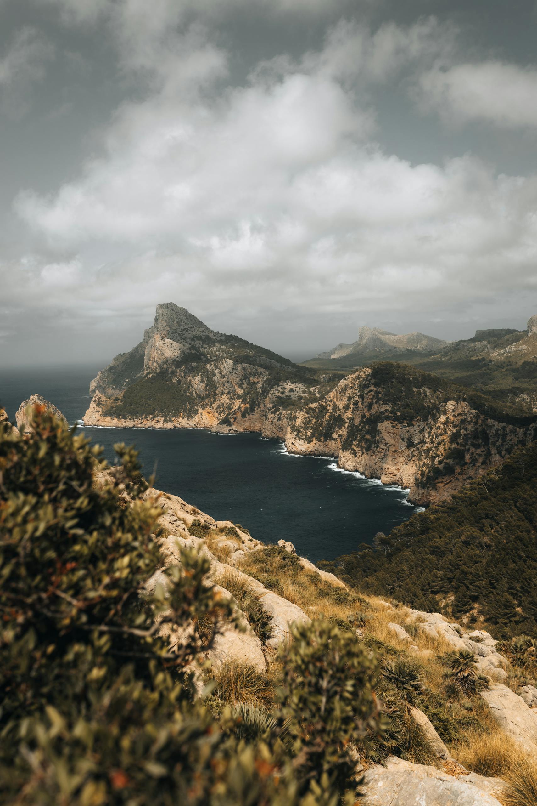 A breathtaking aerial view of Mallorca's rugged cliffs and serene coastline under a cloudy sky.