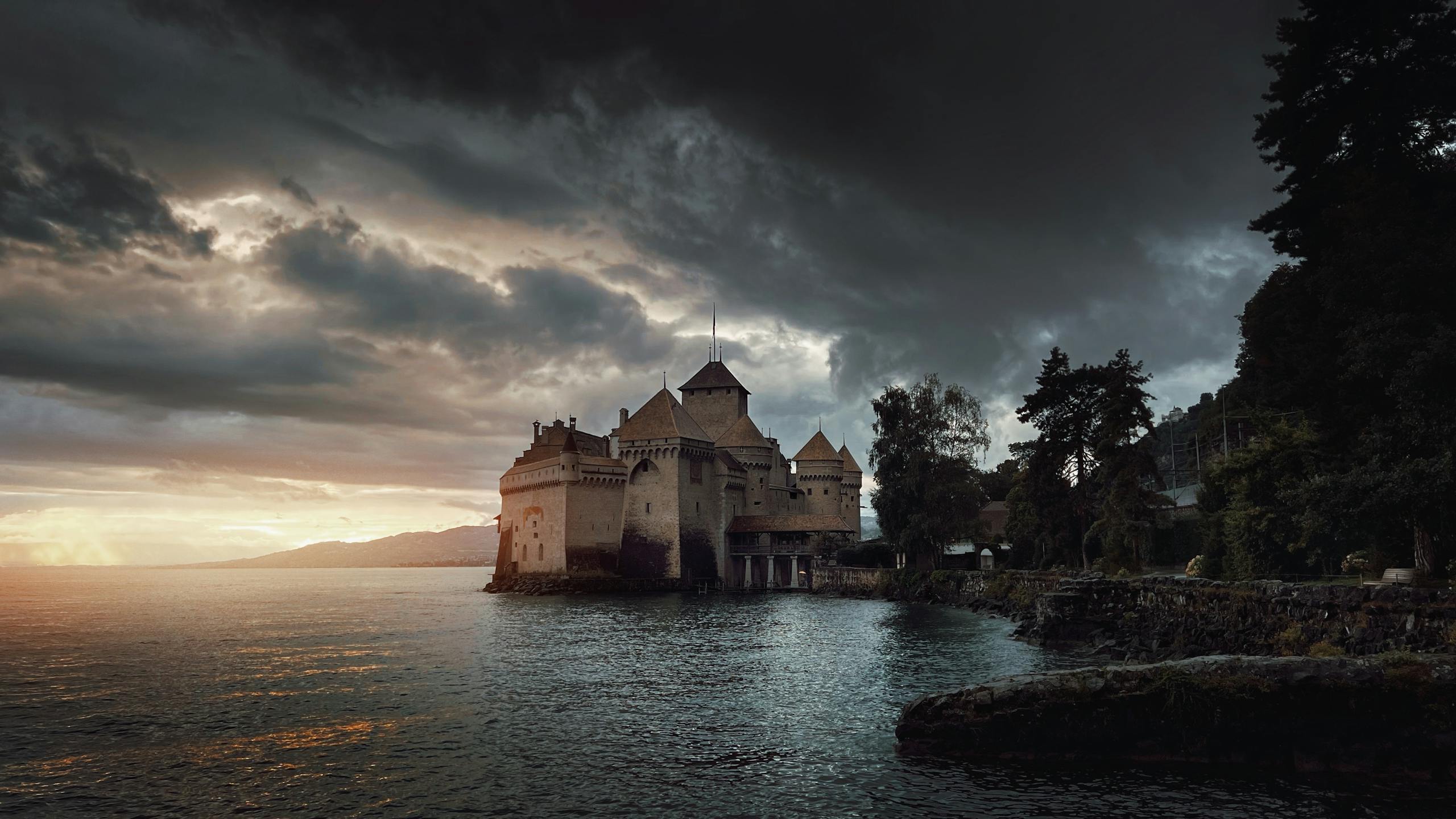 Dramatic view of Chillon Castle on Lake Geneva during sunset with moody clouds.