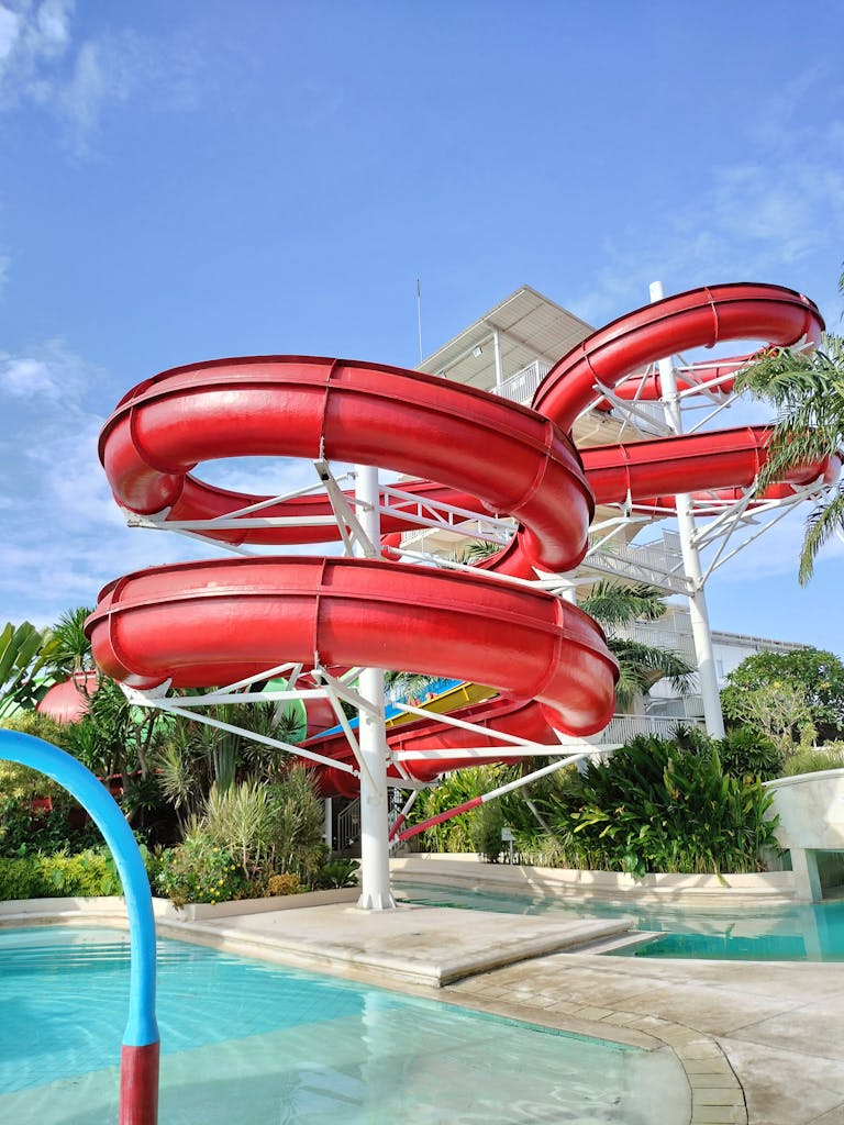 Red water slides in a tropical waterpark under a clear blue sky.