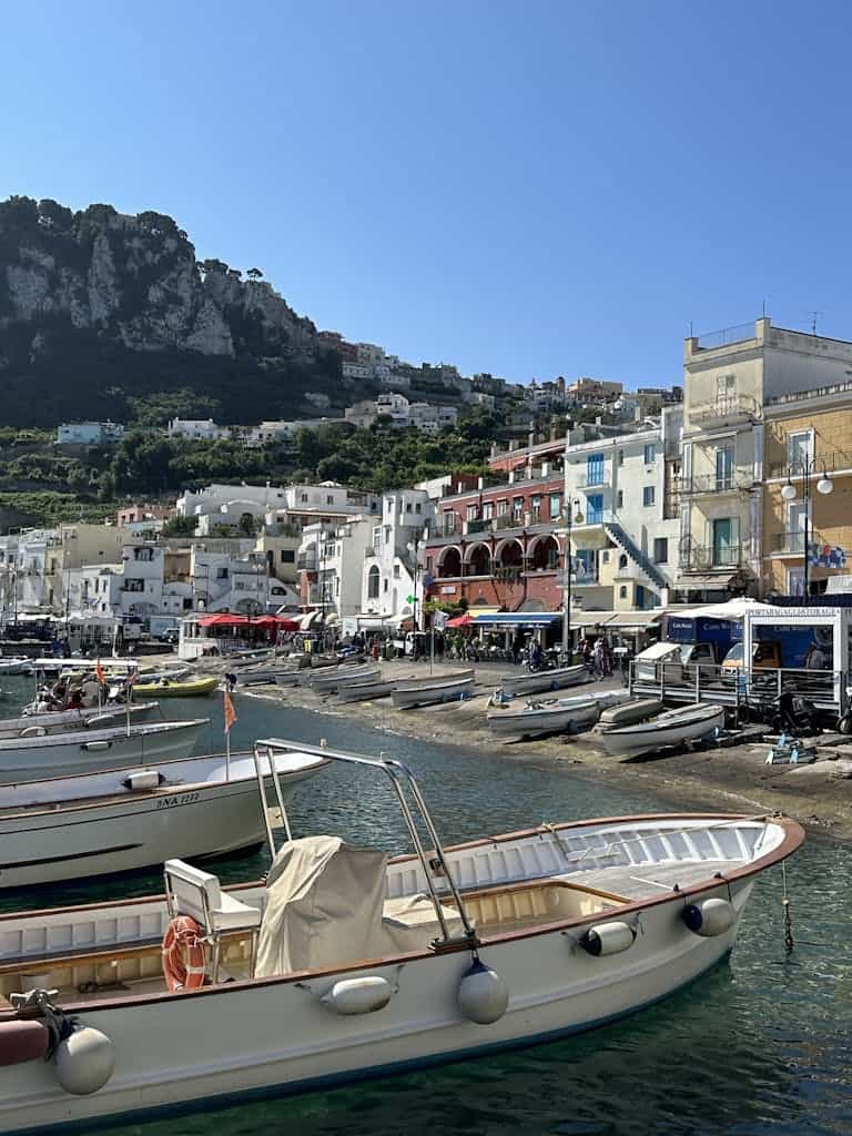 Boats docked at the picturesque marina in Capri, Italy, with vibrant hillside architecture.