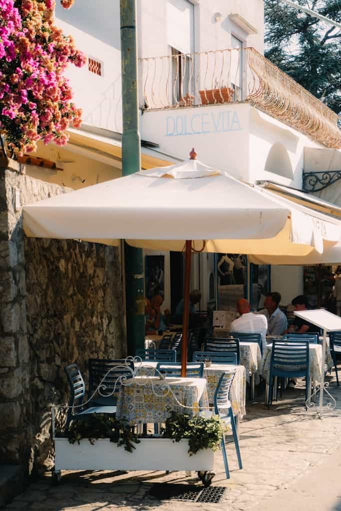 Idyllic outdoor cafe scene in Capri, Italy, capturing a sunny summer day with vibrant flowers and people dining.