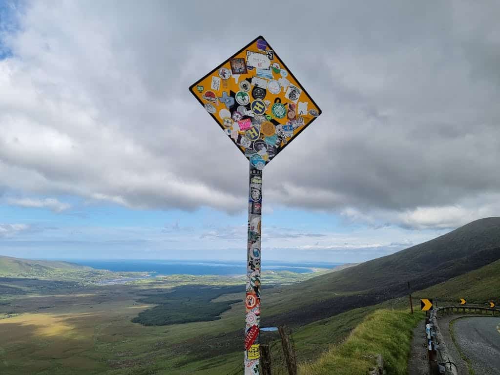 A sticker-covered road sign with a stunning view from Conor Pass, Ireland.