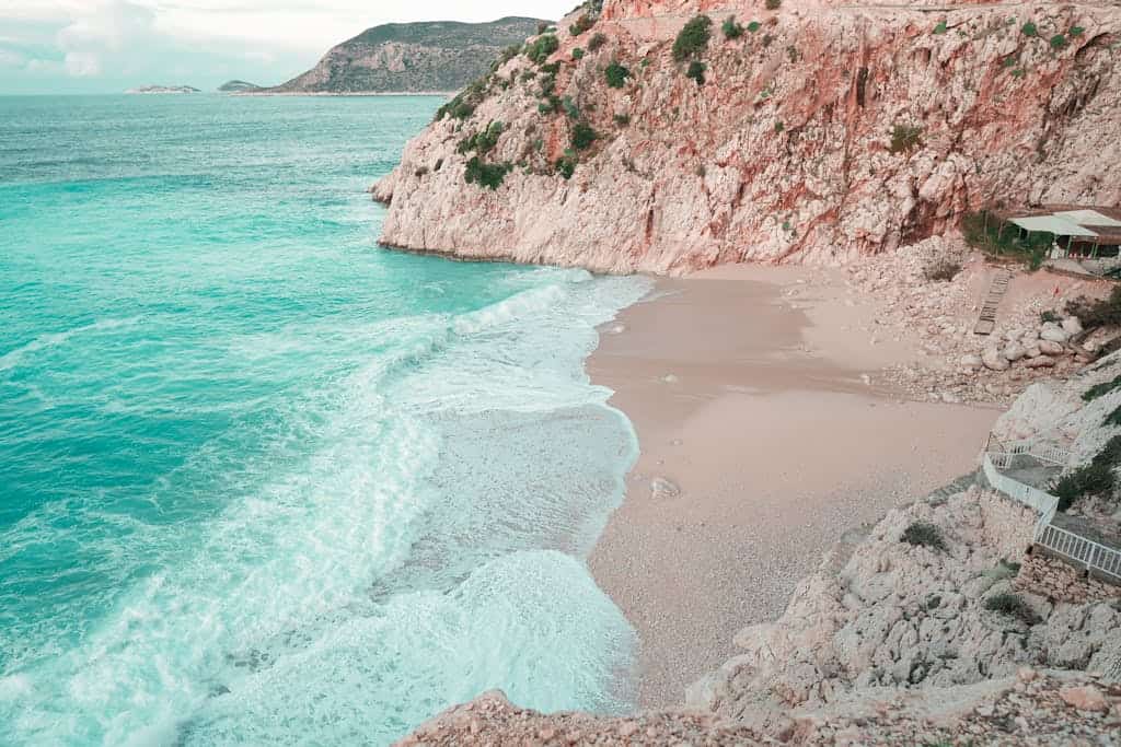Serene view of sandy beach with waves crashing against rocky cliffs in Antalya, Türkiye.