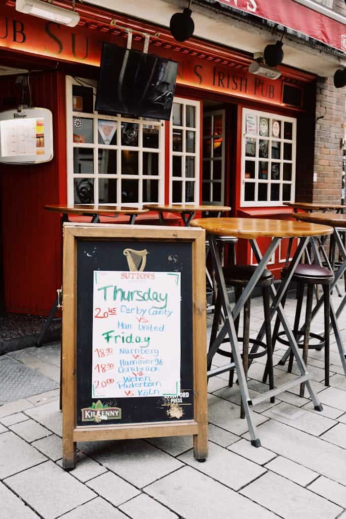 Exterior of empty pub street terrace with high wooden tables and chairs placed on pavement near windows in street of city