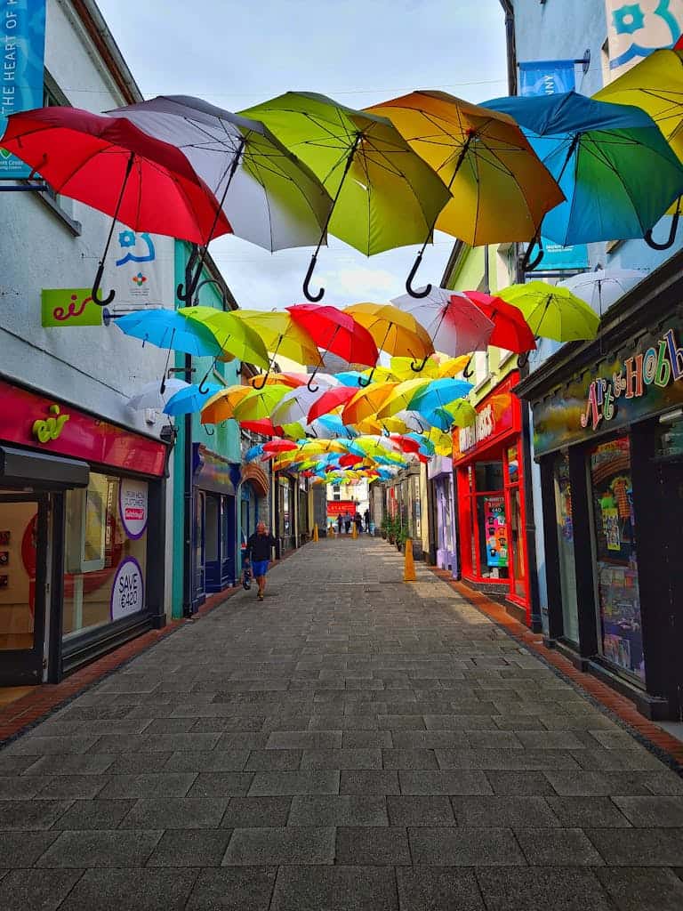 Vibrant multicolored umbrellas hang above a pedestrian street in Kilkenny, creating a lively atmosphere.