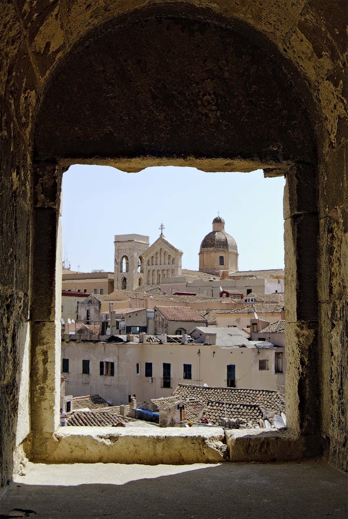 Captivating architectural view of Cagliari cityscape framed through a stone window arch.