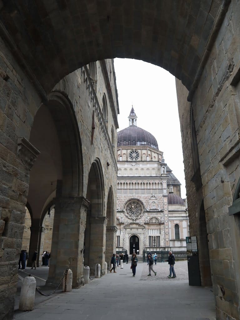 Discover the historical Cappella Colleoni through a picturesque archway in Bergamo, Italy.