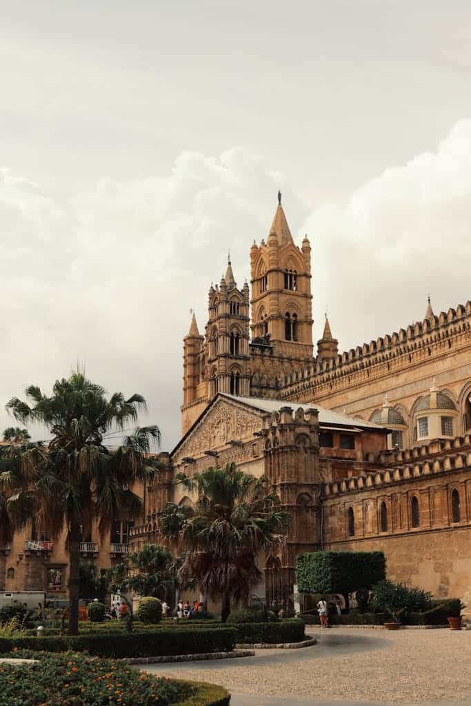 Explore the majestic architecture of Palermo Cathedral surrounded by palm trees in a bustling square.