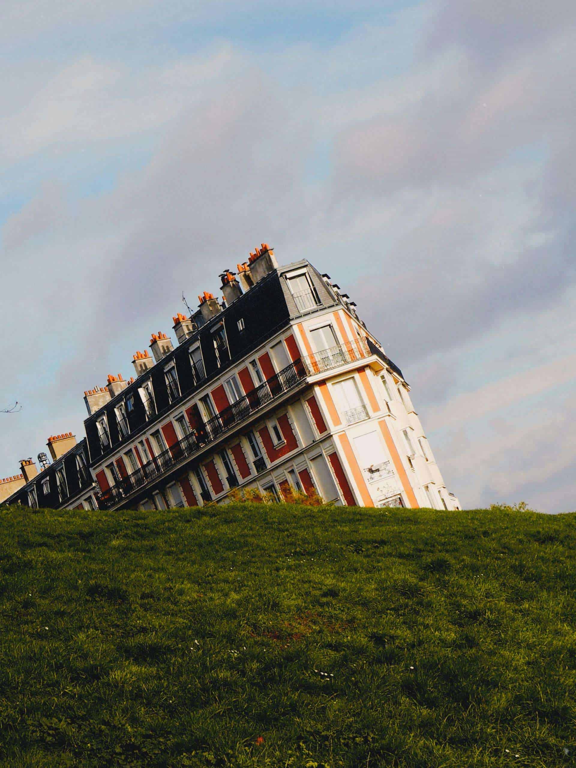 Scenic view of a tilted building in Montmartre, Paris, with green grass and a cloudy sky.
