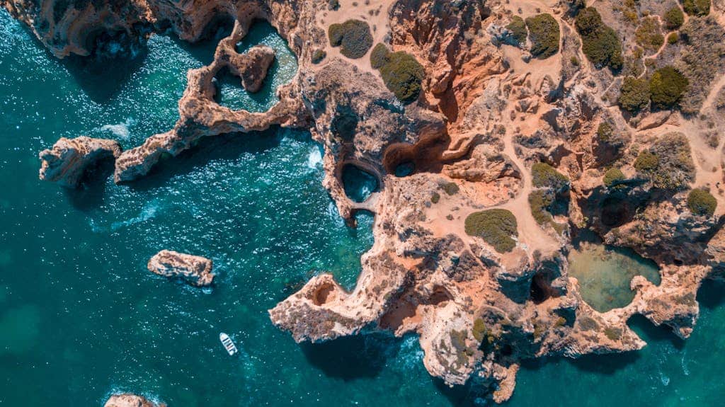 Aerial photograph of the Algarve's rocky coast and turquoise waters with a lone boat.