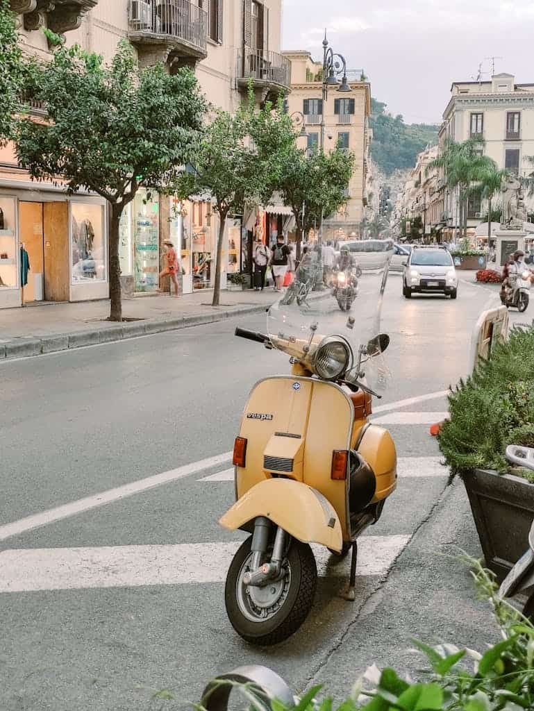 Charming street scene in Sorrento, Italy, with a classic scooter parked against a backdrop of bustling urban life.