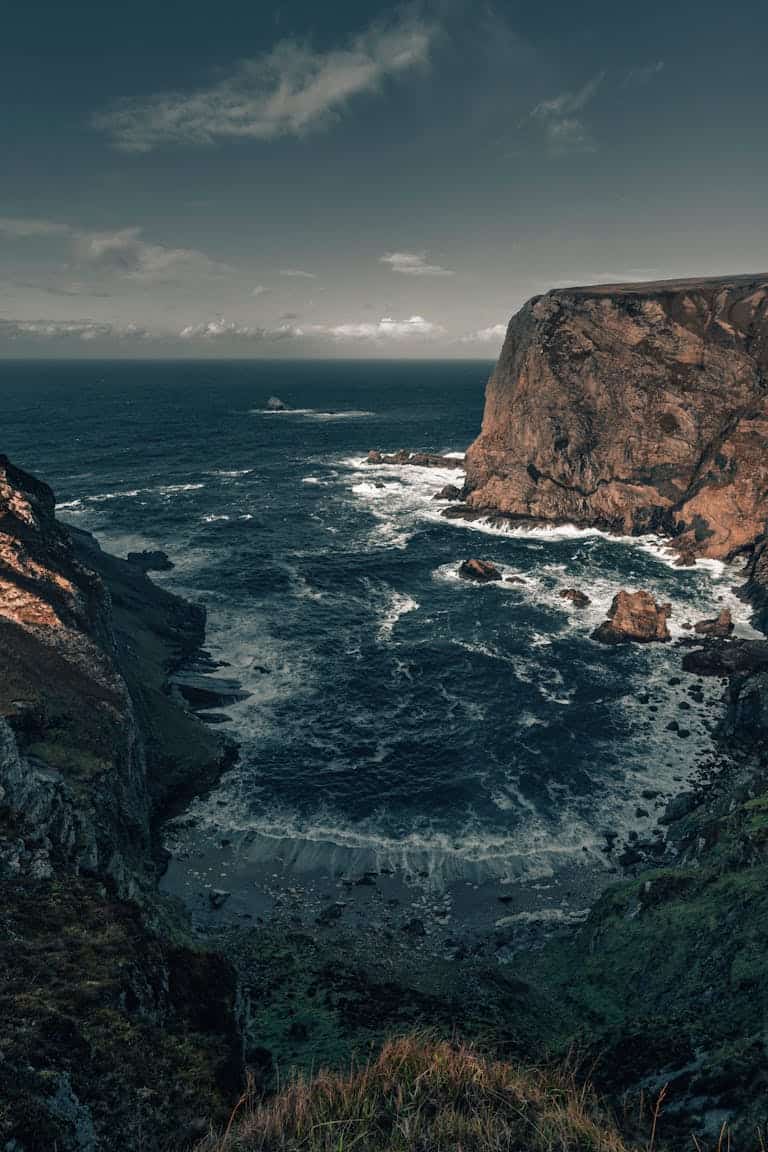 Majestic view of Ireland's coastal cliffs and Atlantic Ocean waves under a cloudy sky.