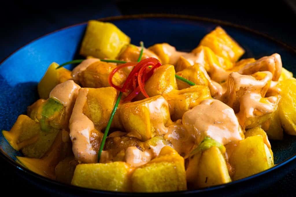 Close-up of patatas bravas with spicy aioli in a vibrant blue bowl.